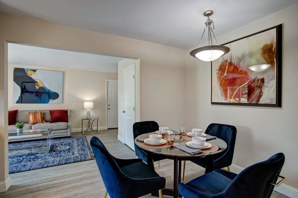 A dining room with a table set for four and a painting on the wall.